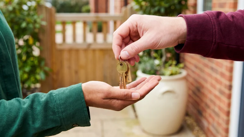 close up of a hand held open with keys to a house being dropped into them by another persons use normal bricks not the glazed green ones hand, used a mixed race hand and white hand - need to be front door key on it as well, and thgey need to be outside not inside the house