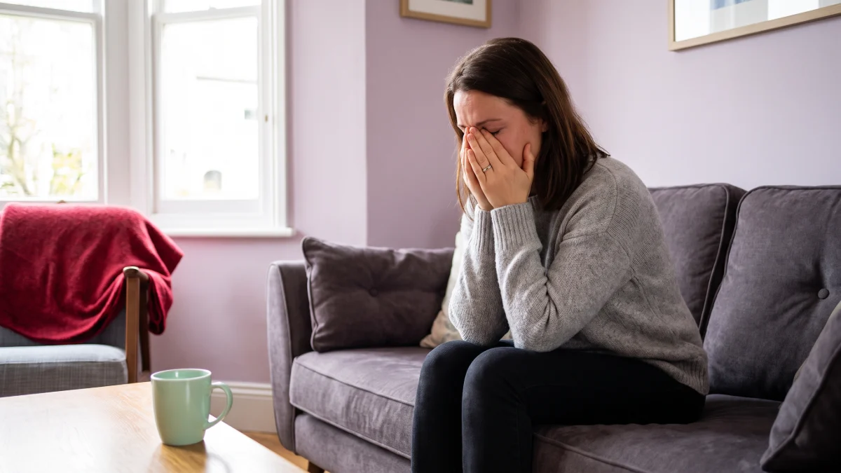 A woman sat crying on the sofa holding her face as if she has been struck