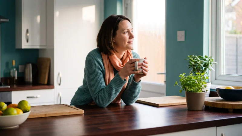 A woman in her thirties standing at a mahogany  kitchen counter in the early evening,